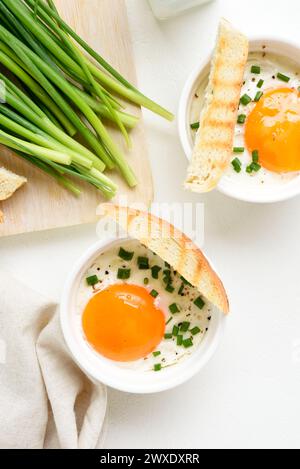 Gebackene Eier mit leuchtendem Orange-Eigelb, serviert mit gegrillten Brotscheiben zum Dippen und frischen grünen Zwiebeln in Portionsschale auf weißem Hintergrund. T Stockfoto