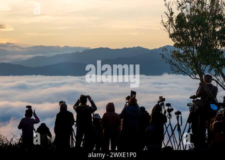 Erleben Sie die ruhigen Momente vor Sonnenaufgang mit dynamischen Wolkenformationen und einer Kulisse aus Neonlichtern vor geschichteten Bergketten. Xindian, Tai Stockfoto