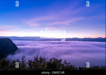 Erleben Sie die ruhigen Momente vor Sonnenaufgang mit dynamischen Wolkenformationen und einer Kulisse aus Neonlichtern vor geschichteten Bergketten. Xindian, Tai Stockfoto