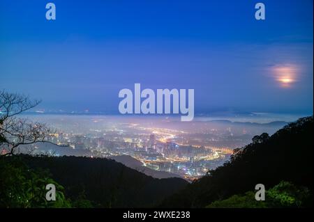 Eine Schicht weißer Wolken und Nebel über Taipeh City bilden zusammen mit den Lichtern der Stadt ein farbenfrohes glasiertes Licht. Der bezaubernde Halbmond hängt in der Th Stockfoto