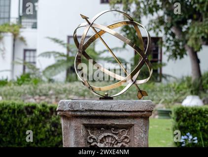 Große armillarische Sonnenuhr aus Messing oder Bronze mit erhöhten römischen Ziffern und Pfeil auf Sockel, Steinsockel mit Muster. Hotelhinterhof, Garten Stockfoto