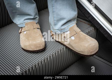 Nahaufnahme von Männerfüßen in beigefarbenem Birkenstock Boston auf der Rolltreppe am 16. März 2024 in Bangkok, Thailand. Stockfoto