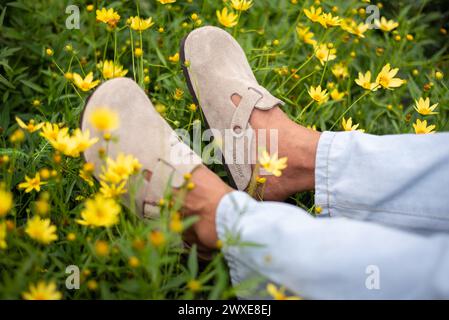 Nahaufnahme von Menschenfüßen in beigefarbenem Birkenstock Boston zwischen Blumen am 16. März 2024 in Bangkok, Thailand. Stockfoto