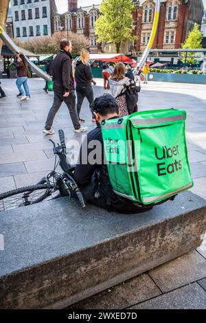 Ein Lieferfahrer für Uber Eats (UberEats) sitzt mit seinem Fahrrad (Fahrrad). Illustration der Uber-Plattformen für die Lieferung von Lebensmitteln zu Hause in Cardiff, Großbritannien Stockfoto