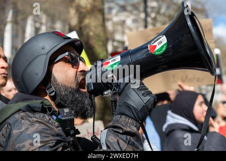 The Strand, London, Großbritannien. 30. März 2024. Während der Konflikt zwischen Israel und der Hamas anhält, findet ein Protest gegen die Eskalation der militärischen Aktionen im Gazastreifen statt. Organisiert von Gruppen wie der palästinensischen Solidaritätskampagne und der „Stop the war Coalition“ mit dem Titel „nationale Demonstration“ und mit Aufrufen zu „Stop the Genocide“, „Ceasefire Now“ und „Free Palestine“, brachen die Demonstranten vom Russell Square auf, bevor sie zum Trafalgar Square fuhren. Männlich in paramilitärischer Uniform mit Megaphon. FOA Stockfoto