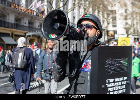 The Strand, London, Großbritannien. 30. März 2024. Während der Konflikt zwischen Israel und der Hamas anhält, findet ein Protest gegen die Eskalation der militärischen Aktionen im Gazastreifen statt. Organisiert von Gruppen wie der palästinensischen Solidaritätskampagne und der „Stop the war Coalition“ mit dem Titel „nationale Demonstration“ und mit Aufrufen zu „Stop the Genocide“, „Ceasefire Now“ und „Free Palestine“, brachen die Demonstranten vom Russell Square auf, bevor sie zum Trafalgar Square fuhren. Männlich in paramilitärischer Uniform mit Megaphon. FOA Stockfoto