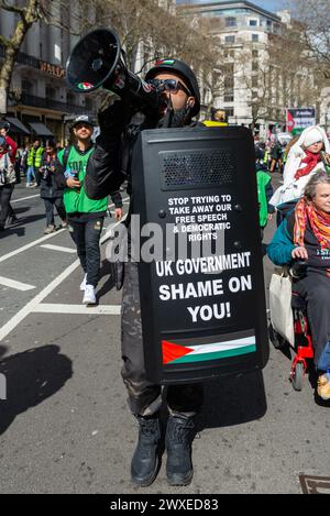 The Strand, London, Großbritannien. 30. März 2024. Während der Konflikt zwischen Israel und der Hamas anhält, findet ein Protest gegen die Eskalation der militärischen Aktionen im Gazastreifen statt. Organisiert von Gruppen wie der palästinensischen Solidaritätskampagne und der „Stop the war Coalition“ mit dem Titel „nationale Demonstration“ und mit Aufrufen zu „Stop the Genocide“, „Ceasefire Now“ und „Free Palestine“, brachen die Demonstranten vom Russell Square auf, bevor sie zum Trafalgar Square fuhren. Männlich in paramilitärischer Uniform mit Megaphon. FOA Stockfoto