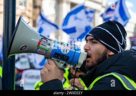 The Strand, London, Großbritannien. 30. März 2024. Während der Konflikt zwischen Israel und der Hamas anhält, findet ein Protest gegen die Eskalation der militärischen Aktionen im Gazastreifen statt. Organisiert von Gruppen wie der palästinensischen Solidaritätskampagne und der „Stop the war Coalition“ mit dem Titel „nationale Demonstration“ und mit Aufrufen zu „Stop the Genocide“, „Ceasefire Now“ und „Free Palestine“, brachen die Demonstranten vom Russell Square auf, bevor sie zum Trafalgar Square fuhren. Sie haben einen israelischen Gegenprotest von The Strand abgegeben. Demonstrant singt durch Megaphon mit Boykott Israel Apartheid Stockfoto