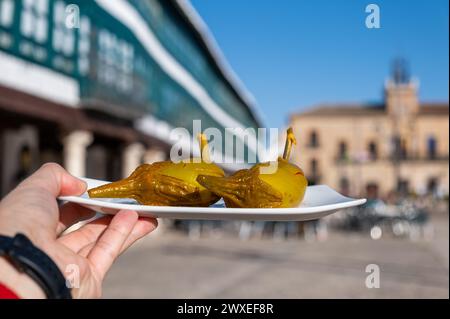 Die Hand eines Mannes zeigt ein typisches Gericht des Almagro in Castilla la Mancha, mit Auberginen, die Berenjenas de Almagro genannt werden, wobei der Hauptplatz außer Fokus steht Stockfoto