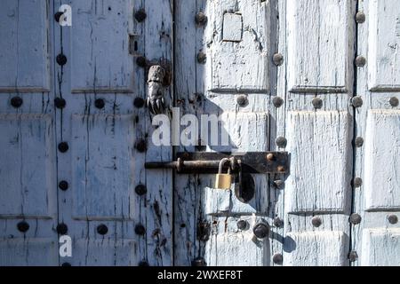 Vorderansicht des Klopfers einer alten blau lackierten Holztür mit rostigen Eisenbeschlägen und Schlossansicht des Klopfers einer alten blau lackierten Holztür Stockfoto