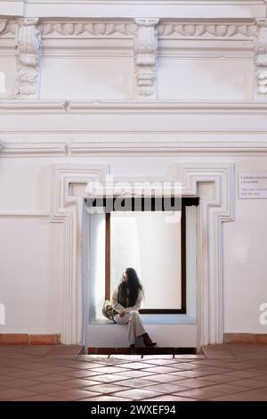 Eine Frau mittleren Alters mit Hut ruht von ihrem Besichtigungstag in einem der Räume der Kirche San Agustin in Almagro, Ciudad Real, Spanien. T Stockfoto