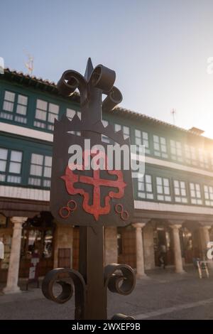 Eisen geschaffenes Emblem des Ordens von Calatrava, beleuchtet von der Morgensonne. Rotes griechisches Kreuz mit Fleur-de-Lis an seinen Enden, auf der Plaza Mayor von Almagro Stockfoto