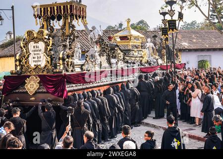 Antigua, Guatemala. März 2024. Katholische Pönitenten tragen den massiven Senor Sepultado-Prozessionszug zu Beginn der Karfreitagsprozession während der Semana Santa, 29. März 2024 in Antigua, Guatemala, durch das historische Stadtzentrum. Die opulente Prozession ist eine der größten der Welt und erfordert über 100 Personen, um den Wagen zu tragen. Die Prozession dauert 12 Stunden. Quelle: Richard Ellis/Richard Ellis/Alamy Live News Stockfoto