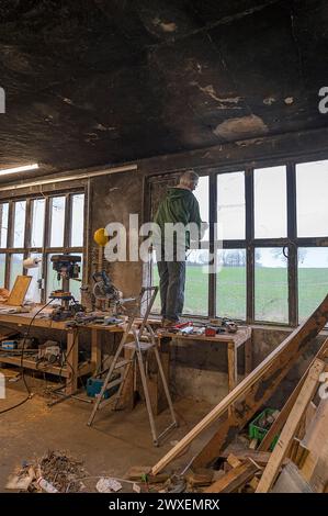 Älterer Mann, der auf einer Werkbank steht und ein Fenster in einer Werkstatt repariert, Mecklenburg-Vorpommern Stockfoto