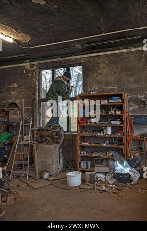 Älterer Mann, der auf einer Schleifmaschine steht und ein Fenster repariert, in einer Werkstatt, Mecklenburg-Vorpommern Stockfoto