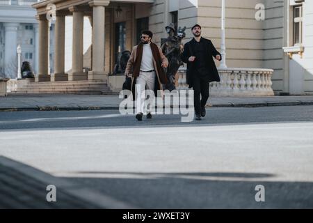 Dynamisches Bild von zwei jungen Berufstätigen, die mit einem Gefühl der Dringlichkeit über eine Straße eilen und damit die Geschäftstätigkeit in einem städtischen Umfeld symbolisieren. Stockfoto