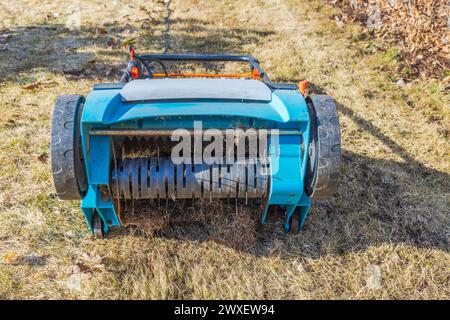 Nahaufnahme eines elektrischen Rasenbelüfters mit Stacheldrahtdüse auf gelbem Gras in einem Garten an einem Frühlingstag in Schweden. Stockfoto