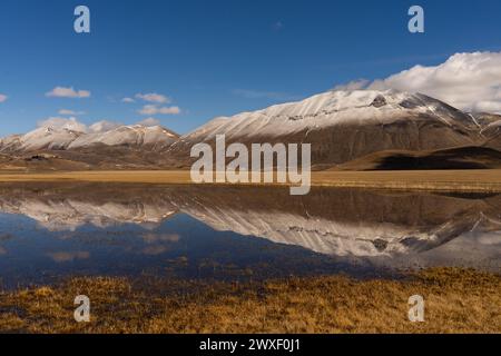 UNO specchio d'acqua riflette le montagne scarsamente Innevate, creando un'atmosfera suggestiva ai piedi del Monte Vettore Stockfoto