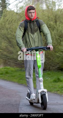 Milton Keynes, UK-Mar 30th 2024: Junger Mann auf einem Elektroroller vor grüner Kulisse Stockfoto