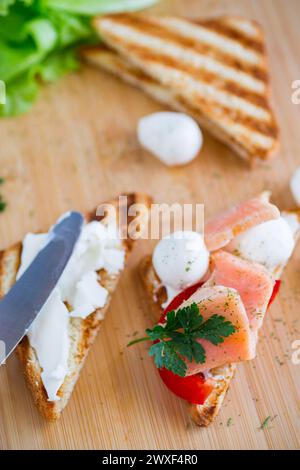 Gebratener Toast mit Lachs, Frischkäse, Salat, auf einem Holztisch Stockfoto