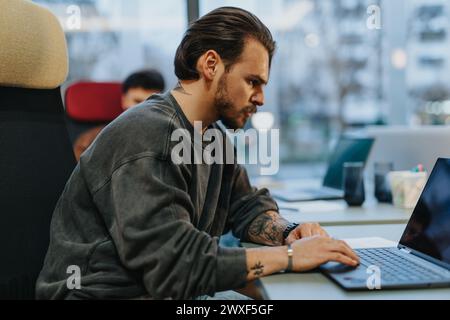 Junger Mann, der auf dem Laptop am Schreibtisch neben dem Fenster arbeitet. Stockfoto
