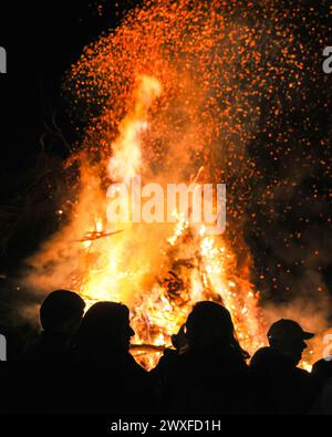 Sythen, NRW, Deutschland. 30. März 2024. Einheimische und Besucher treffen sich zum jährlichen Osterfeuer auf dem Prickingshof in Sythen, Westfalen (Münsterland). Das Anzünden von Osterfeuern ist in Deutschland seit Jahrhunderten Tradition, meist am Karsamstag oder Ostersonntag. Feuerwehr und Rettungsdienste sorgen dafür, dass das Feuer sicher gehalten wird, während Freiwillige das Brennholz sorgfältig inspiziert haben, um sicherzustellen, dass keine Wildtiere in den Zweigen Zuflucht gefunden haben. Quelle: Imageplotter/Alamy Live News Stockfoto