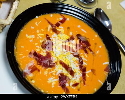 Salmorejo: Tomatensuppenpüree mit Brot, traditionell kalt mit Marmelade und gekochtem Ei in einer schwarzen Schüssel. Andalusische Küche. Stockfoto