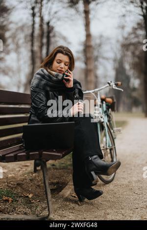 Elegante junge Geschäftsfrau in stilvoller Kleidung, die auf einer Parkbank sitzt Stockfoto