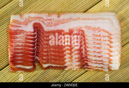 Nahaufnahme dünner Scheiben ausgehärteten Streifenspecks auf Holzoberfläche. Stockfoto