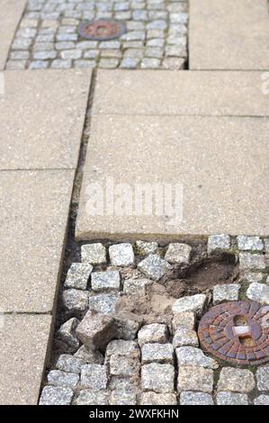 Nahaufnahme des Kopfsteinpflasterpflasters. Die Steine sind ungleichmäßig angeordnet, einige sind verstreut. Konzepte: Städtischer Verfall, beschädigter Bürgersteig, Straßenreparatur, Straßenschäden, alte Pflastersteine Stockfoto