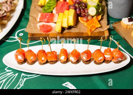 Herzhafte geräucherte Lachsbrötchen mit Frischkäse auf Roggenbrot, auf einem weißen Servierteller bei einer festlichen Veranstaltung. Stockfoto