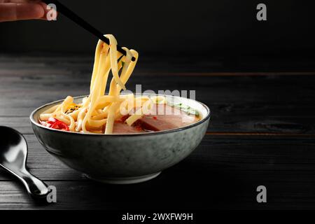 Frau isst köstliche Ramen mit Stäbchen an schwarzem Holztisch, Nahaufnahme und Platz für Text. Nudelsuppe Stockfoto