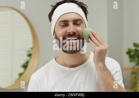 Mann mit Stirnband, der sein Gesicht mit Schwamm im Badezimmer wäscht Stockfoto