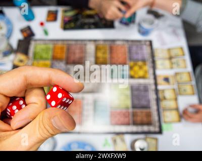 Hand mit roten sechsseitigen Würfeln, die eine vier auf dem Spielbrett von oben zeigen, zusammen mit anderen echten Spielern Stockfoto