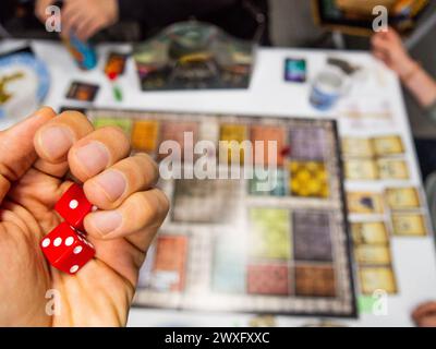 Hand mit roten sechsseitigen Würfeln, die eine und eine drei auf dem Spielbrett von oben zeigen, zusammen mit anderen echten Spielern Stockfoto