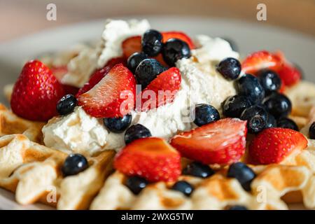 Goldene belgische Waffeln mit Erdbeeren, Heidelbeeren und frisch geschlagener Sahne. Ein köstlicher Genuss bei jedem Happen für ein besonderes Frühstück. Stockfoto