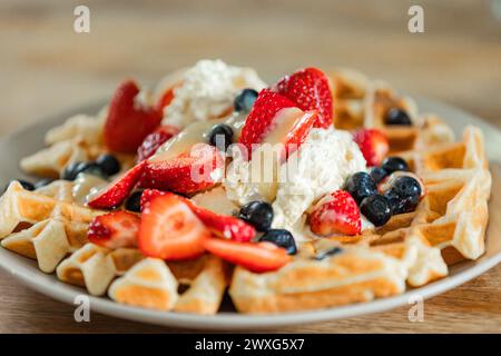 Goldene belgische Waffeln mit Erdbeeren, Heidelbeeren und frisch geschlagener Sahne. Ein köstlicher Genuss bei jedem Happen für ein besonderes Frühstück. Stockfoto