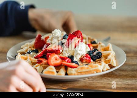 Goldene belgische Waffeln mit Erdbeeren, Heidelbeeren und frisch geschlagener Sahne. Ein köstlicher Genuss bei jedem Happen für ein besonderes Frühstück. Stockfoto