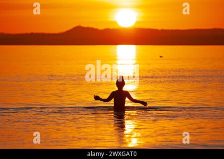 Portobello, Edinburgh, Schottland, Großbritannien. 31. März 2024. Atemberaubender Sonnenaufgang im britischen Sommer an der schottischen Küste sowie Ostersonntag. Im Bild: Weibchen nimmt ein kühles Bad im Firth of Forth bei Sonnenaufgang, Temperatur 6 Grad Celsius. Quelle: Arch White/Alamy Live News. Stockfoto