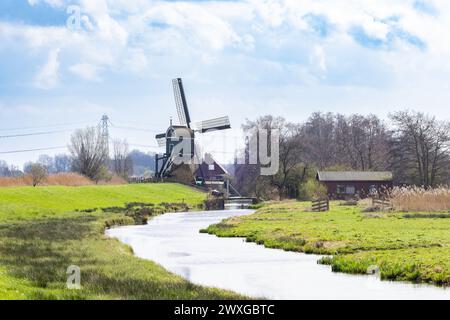 Landschaft mit Deich und historischem Oukoopse molen mit miller's Cottage entlang der Enkel Wiericke in der niederländischen Provinz Zuid Holland gegen einen Hinterhalt Stockfoto