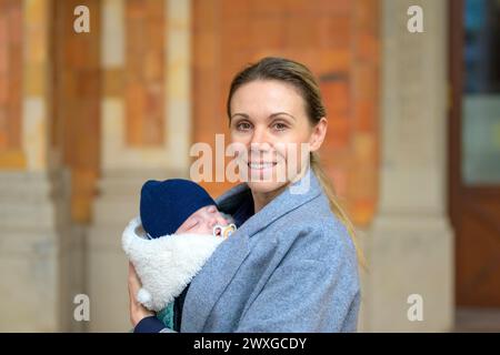 Porträt einer extrem glücklichen Mutter in ihren 40ern, die ihr neugeborenes Baby hält und zur Kamera im Freien lächelt Stockfoto