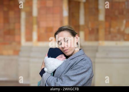 Glückliche spätgeborene Mutter in ihren 40ern hält ihr neugeborenes Baby und beide mit geschlossenen Augen im Freien Stockfoto