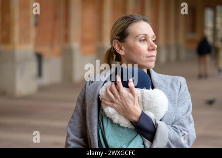 Glückliche, spätgeborene Mutter in ihren 40ern, die ihr neugeborenes Baby hält und nach draußen zufrieden aussieht Stockfoto