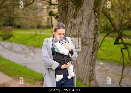 Glückliche Frau küsst ihr Baby, das sie in einer Babytrage im Park hält Stockfoto