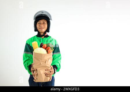 Asiatischer Online-Fahrer mit Uniform und Helm, der frisches Gemüse in Papiertüte liefert, Stockfoto