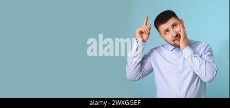 Nachdenklicher junger Geschäftsmann, der etwas auf blauem Hintergrund mit Platz für Text zeigt Stockfoto