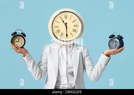 Geschäftsfrau mit Uhr statt Kopf auf hellblauem Hintergrund. Zeitmanagement-Konzept Stockfoto