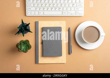 Schreibtisch mit Notizblock, Stift, Tastatur, saftigen Pflanzen und Kaffeetasse auf beigefarbenem Tisch. Draufsicht, flach. Stockfoto