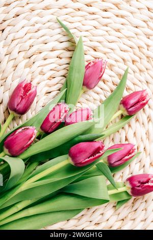 Lila Tulpenblüten auf der Korbmatte. Frühlingsferienkonzept, festlicher Hintergrund. Draufsicht, flach, Kopierbereich. Stockfoto