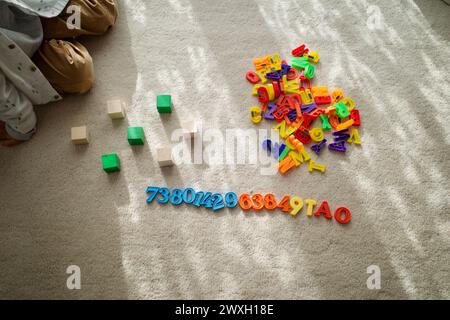 Lernen durch Spielen - ein Kind spielt Zahlen und Buchstabenspielzeug auf einem Teppich. Stockfoto